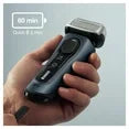 Hand holding a black electric shaver with visible branding on a dark background
