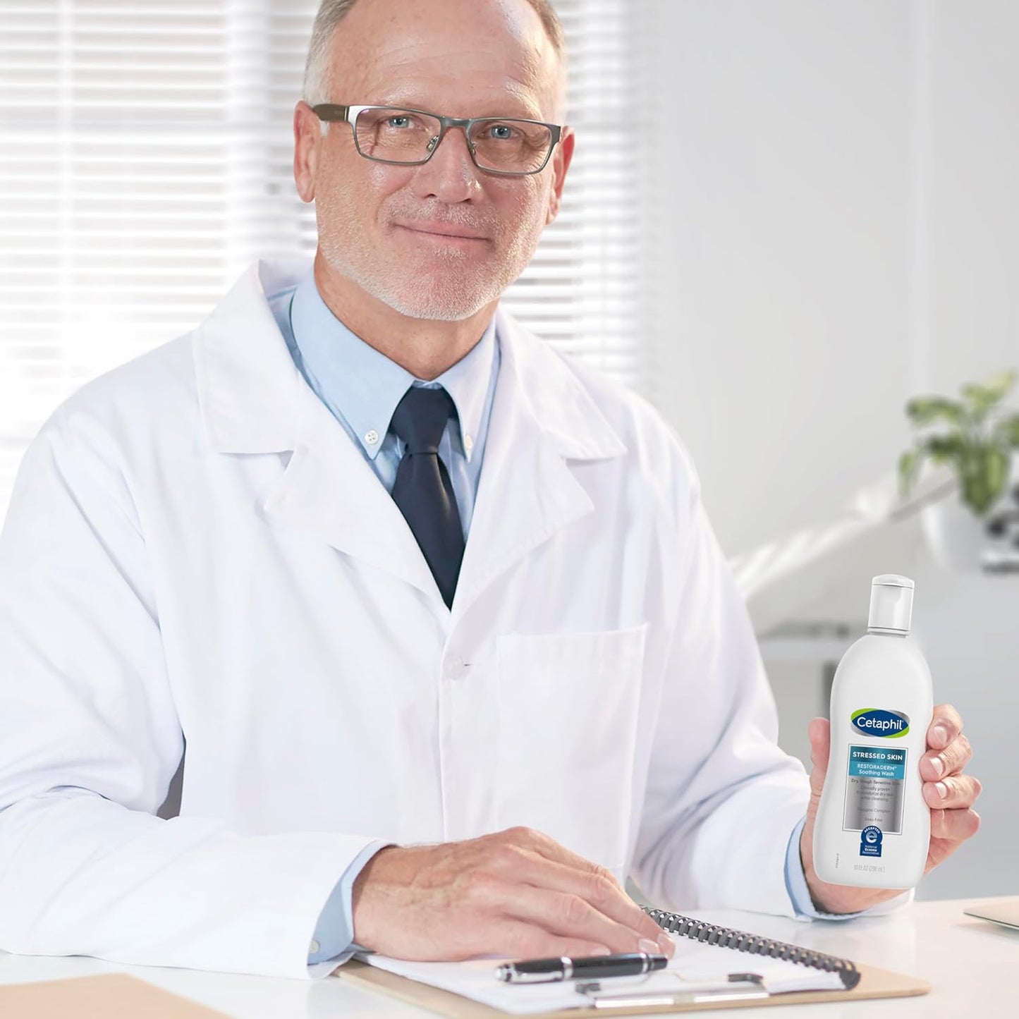 Man in a white lab coat holding a bottle of Cetaphil product in an office setting.