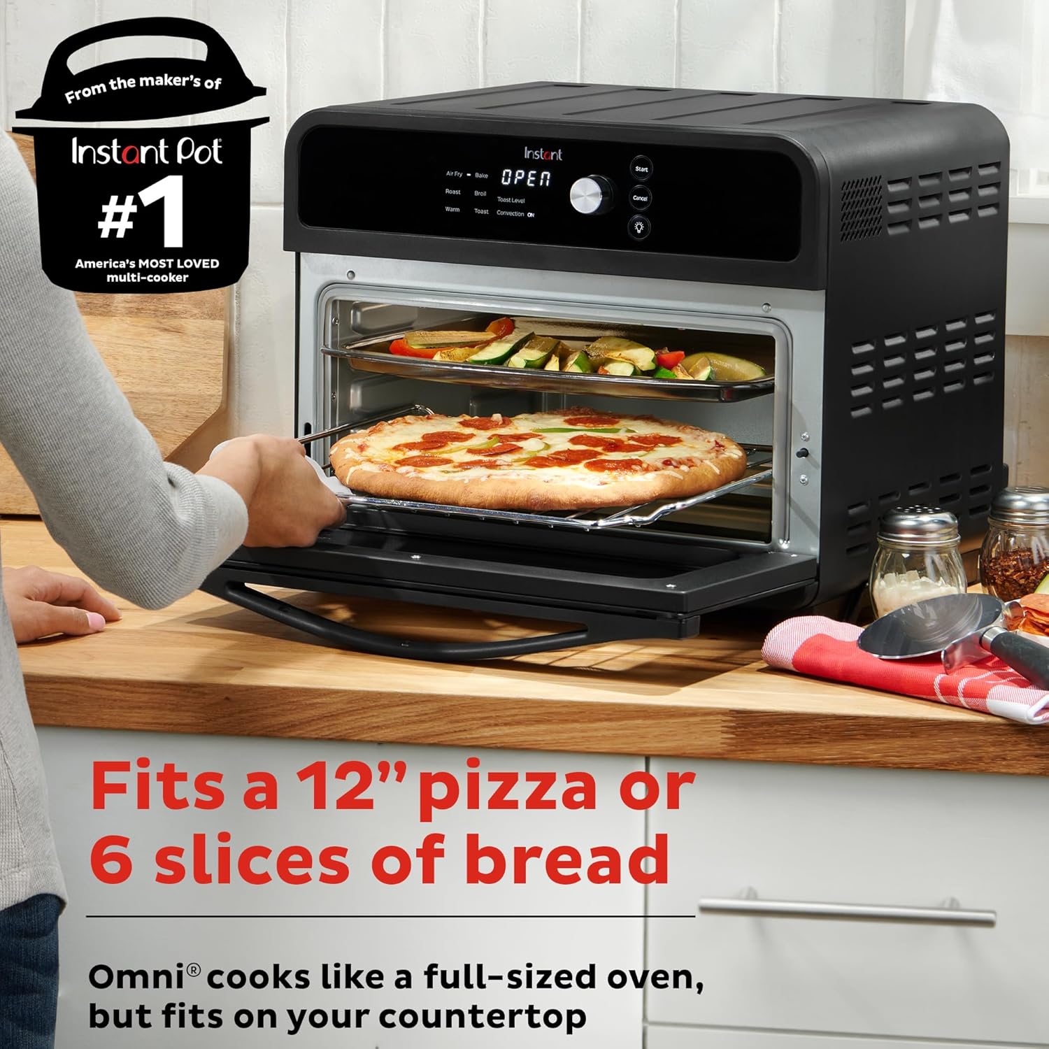 Black countertop oven with pizza being inserted, surrounded by kitchen items.