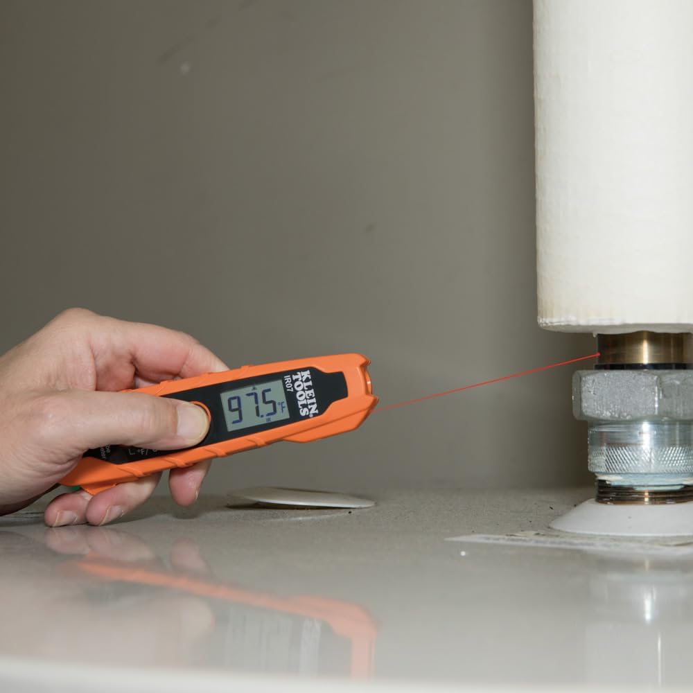 Hand holding a digital thermometer near a pipe with a red laser pointer.