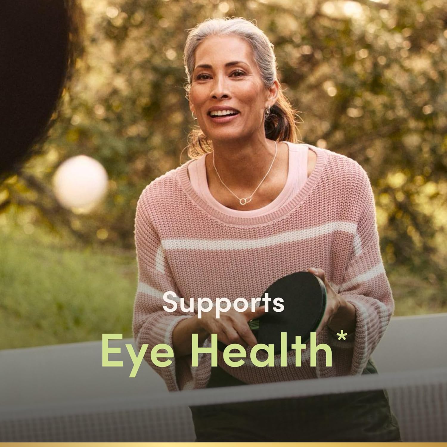 Woman holding a container labeled 'Supports Eye Health' outdoors