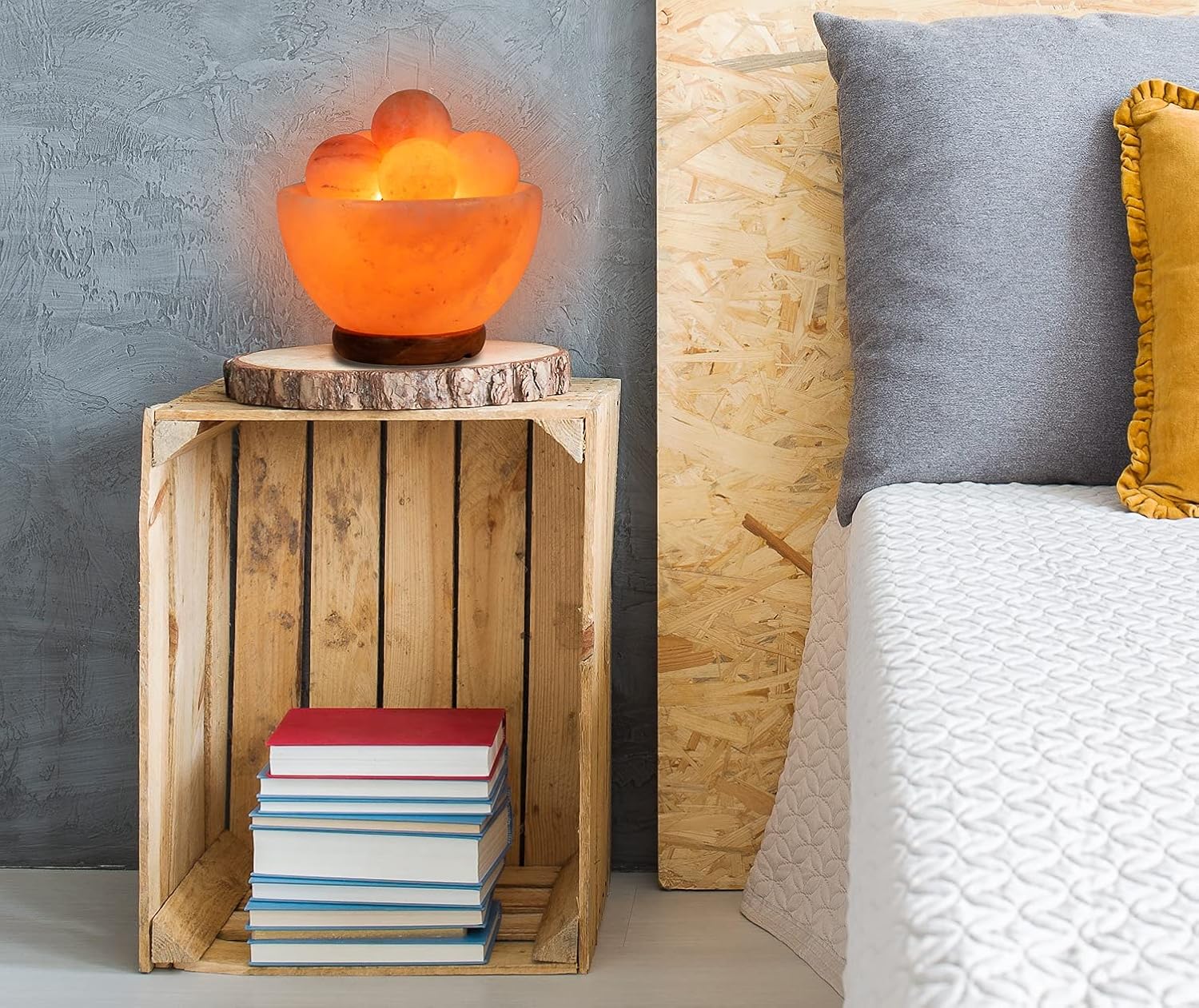 Wooden crate with a lamp and books next to a bed with pillows