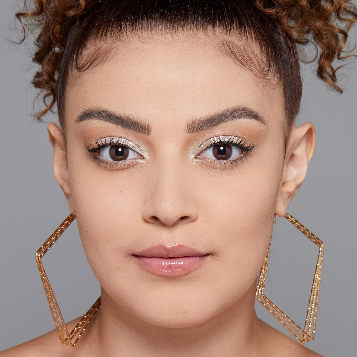 Close-up of a person wearing large gold hoop earrings against a gray background