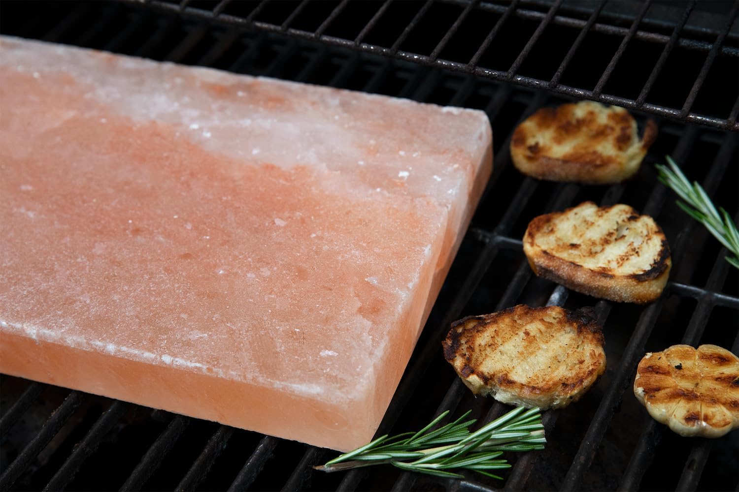 Himalayan salt block on a grill with grilled items and rosemary