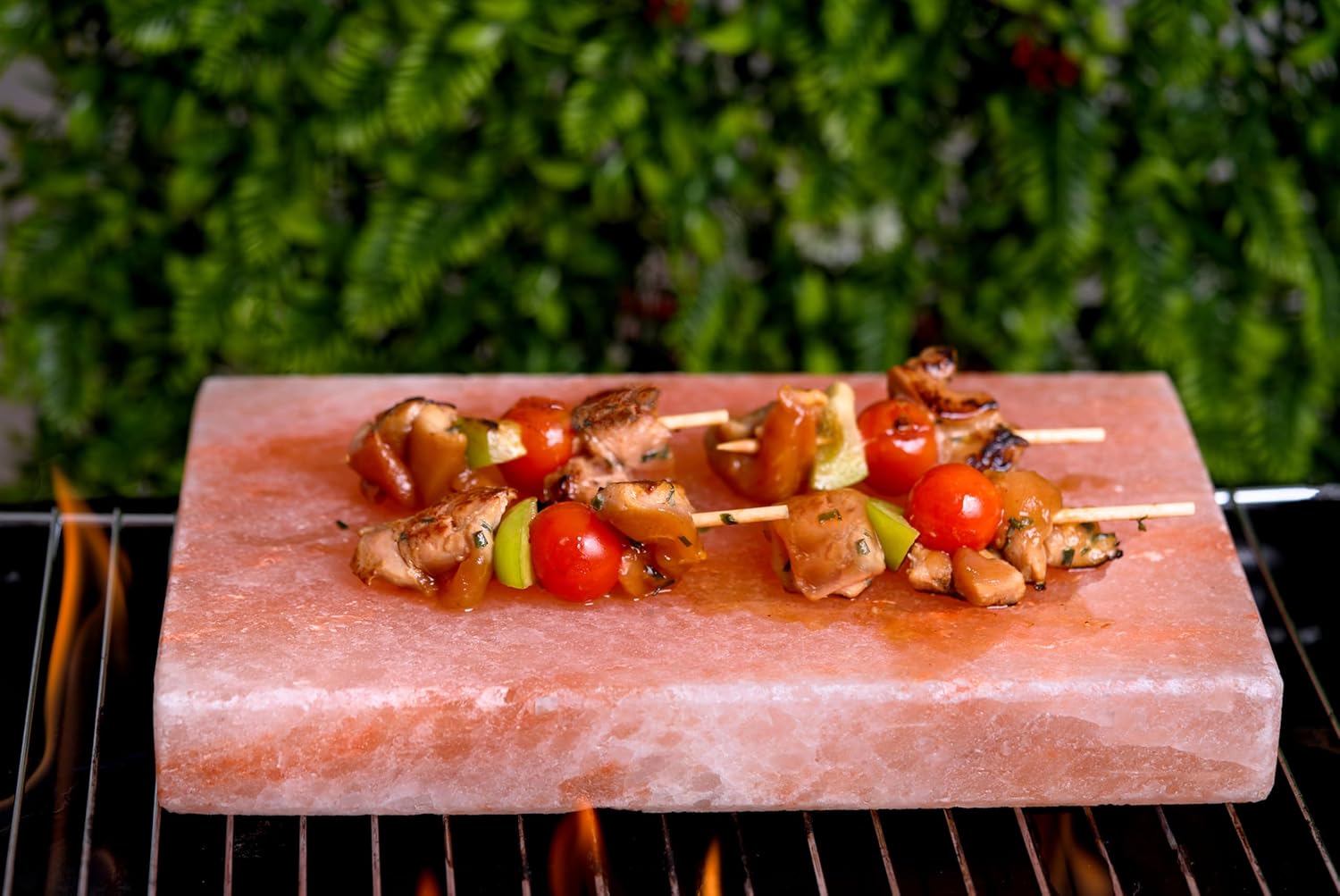 Kebabs on a pink salt block over a grill with a blurred green background