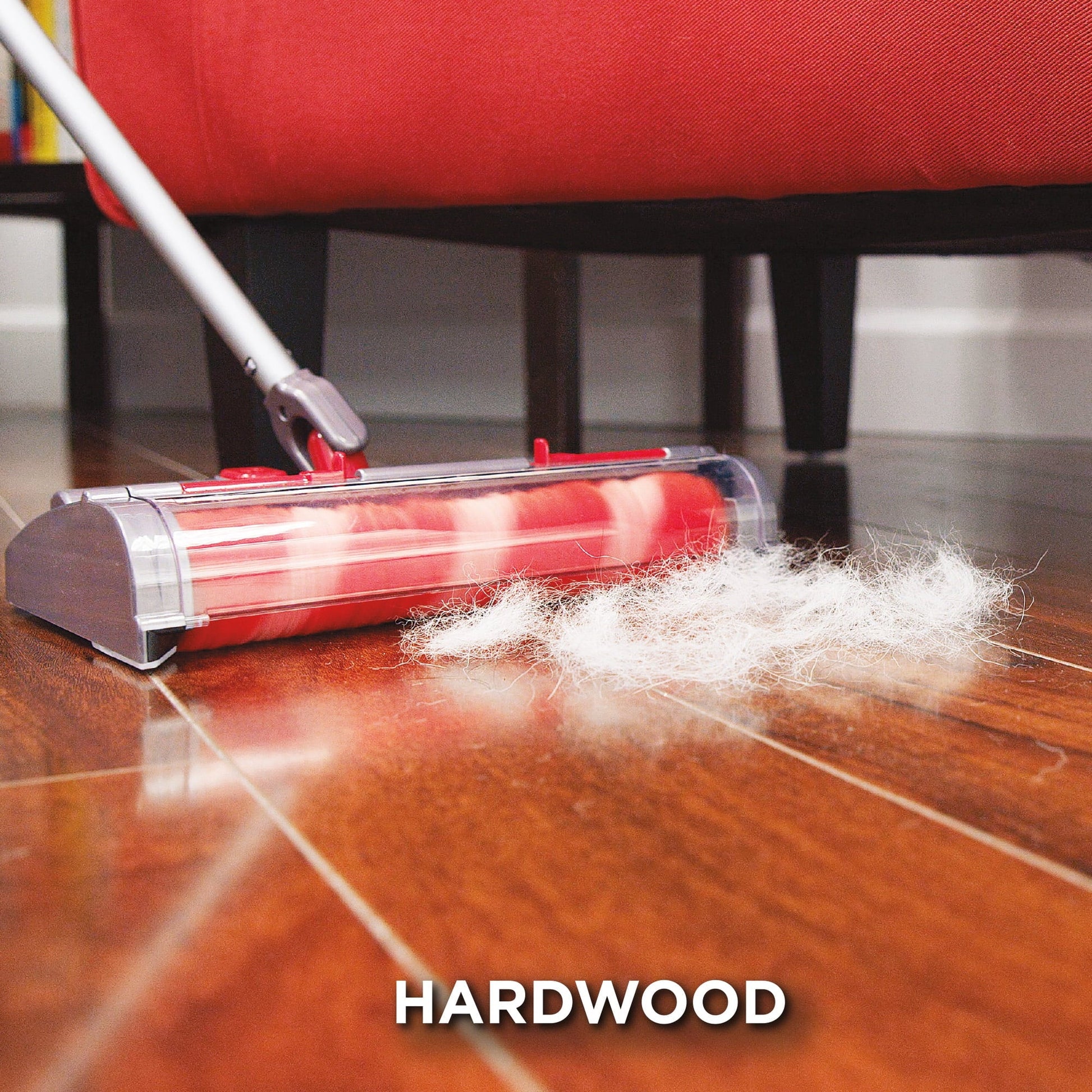 Red vacuum cleaner cleaning a hardwood floor with a red couch in the background.